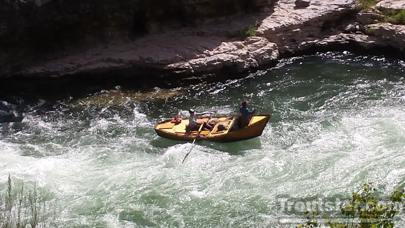 A wooden drift boat running through rapids